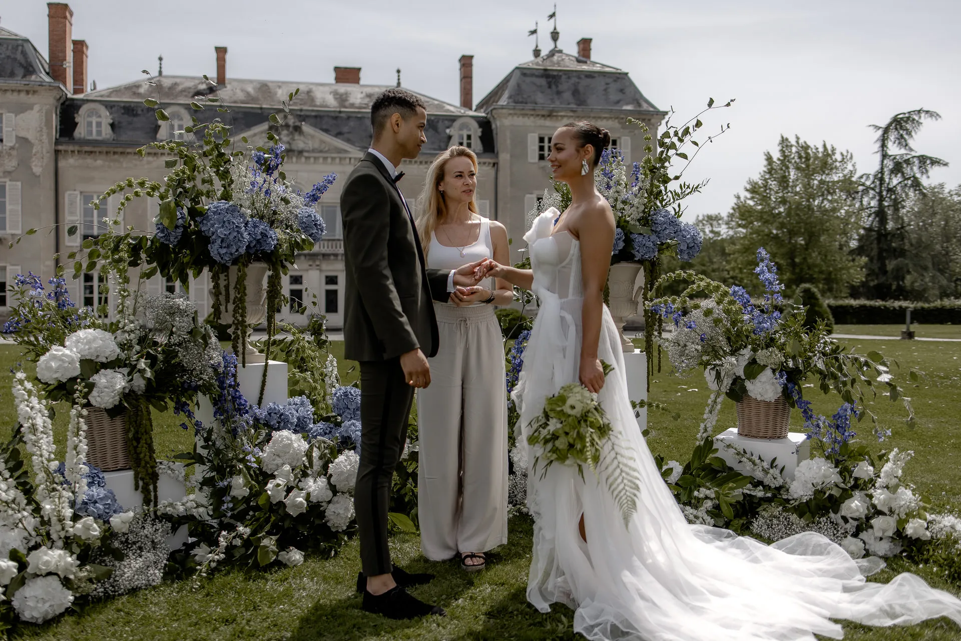 Bridal couple with wedding officiant at ceremony at Chateau de Varennes with blue and white floral decor